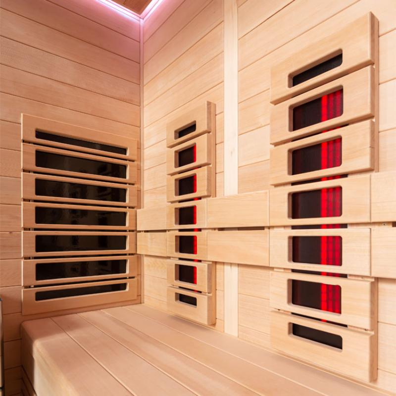 Modernes Infrarotkabinen-Interieur aus Hemlock-Holz mit mehreren Infrarot-Heizelementen in Rot- und Schwarztönen an den Wänden, Rosa-LED-Deckenbeleuchtung und Holzbänken