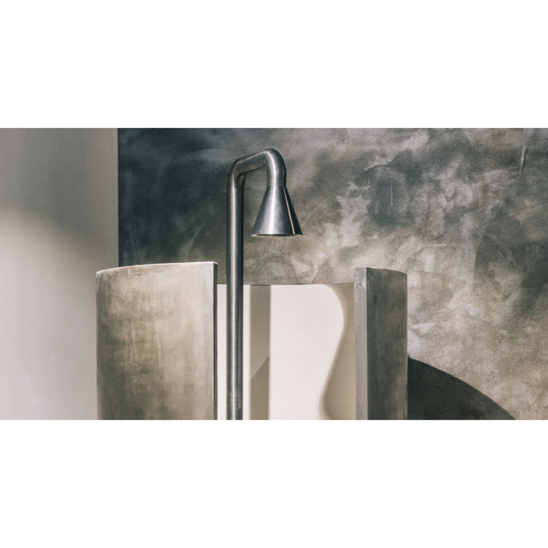 JEE-O cone 01 Gartendusche aus Edelstahl mit geschwungenem Design vor modernem Betonhintergrund und Sichtschutzelementen