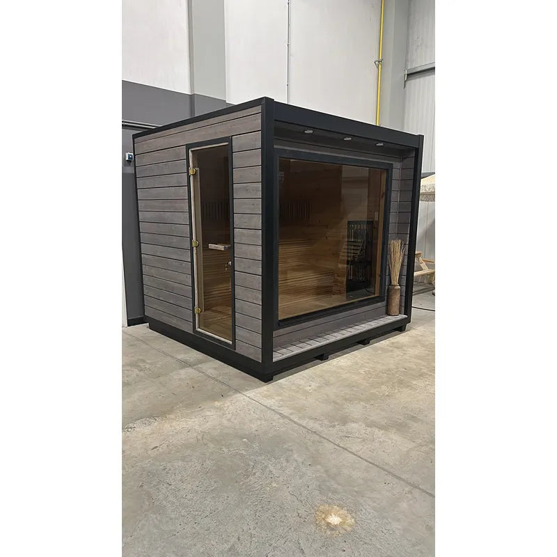 KOBA Cube Gartensauna - Moderne quadratische Form mit schwarzem Rahmen, grauem Holzaußenbau und großem Glasfenster, Innenraum mit Holzbänken sichtbar