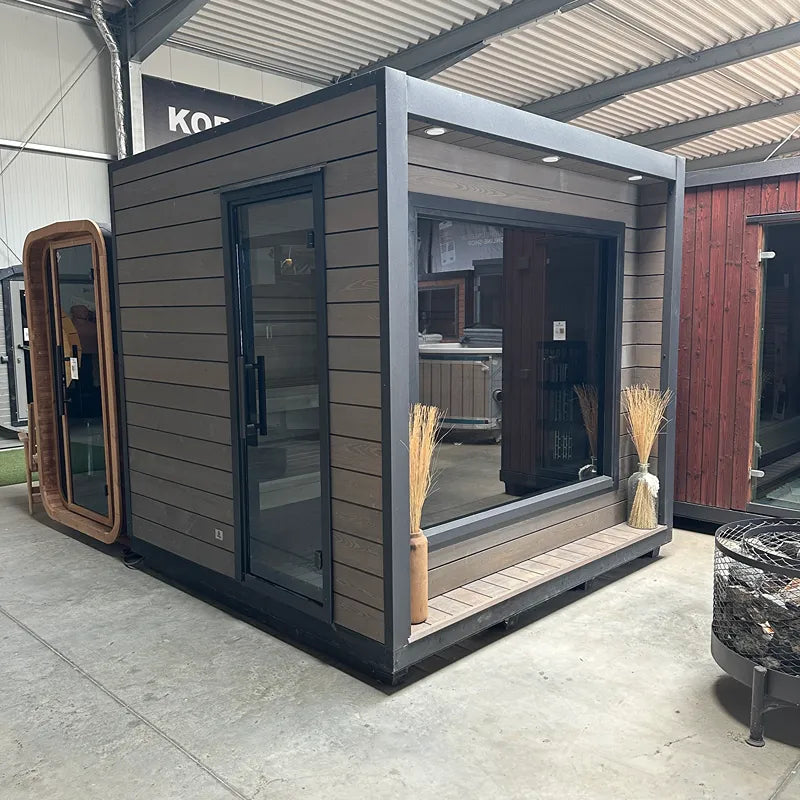 KOBA Cube Gartensauna mit moderner quadratischer Form, schwarze Holzverkleidung und großen Glasfenstern in Ausstellungshalle