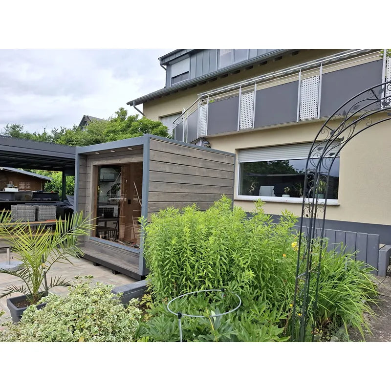 KOBA Cube Gartensauna mit moderner quadratischer Form im Garten neben Terrassenbereich und Bepflanzung