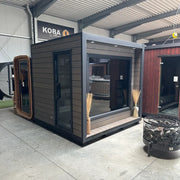 KOBA Cube Gartensauna - Moderne quadratische Form mit schwarzer Holzverkleidung und großen Fenstern in Ausstellungshalle