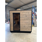 KOBA Cube Gartensauna mit moderner quadratischer Form, Holzfassade und schwarzem Rahmen in Lagerhalle