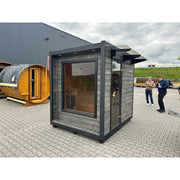 KOBA Cube Gartensauna - Moderne quadratische Form mit grauer Holzfassade und großem Fenster in Ausstellungshof