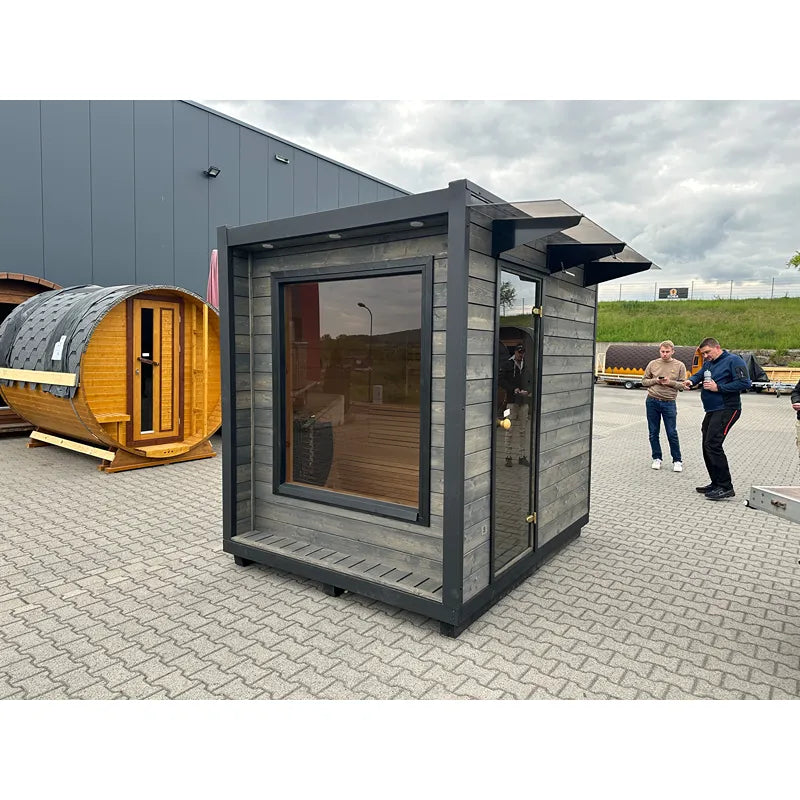KOBA Cube Gartensauna - Moderne quadratische Form mit grauer Holzfassade und großem Fenster in Ausstellungshof