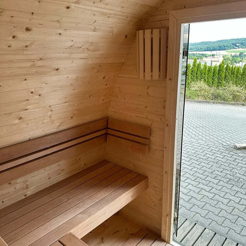 KOBA Iglu Gartensauna Innenraum mit Holzbänken, gewölbtem Holzdach und offener Glastür zum Garten