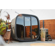 Leil Black Cube Classic Gartensauna 4 Personen mit schwarzem Rahmen und großen Glastüren im modernen Garten
