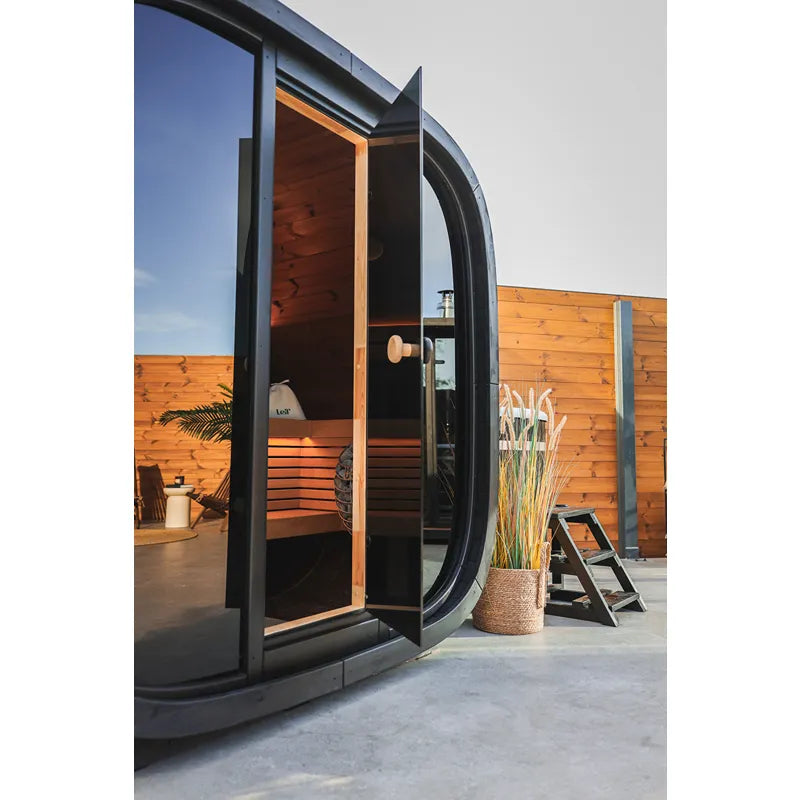 Leil Black Cube Classic Gartensauna 4 Personen mit schwarzem Stahlrahmen, offener Tür und Holzinnenraum im Garten