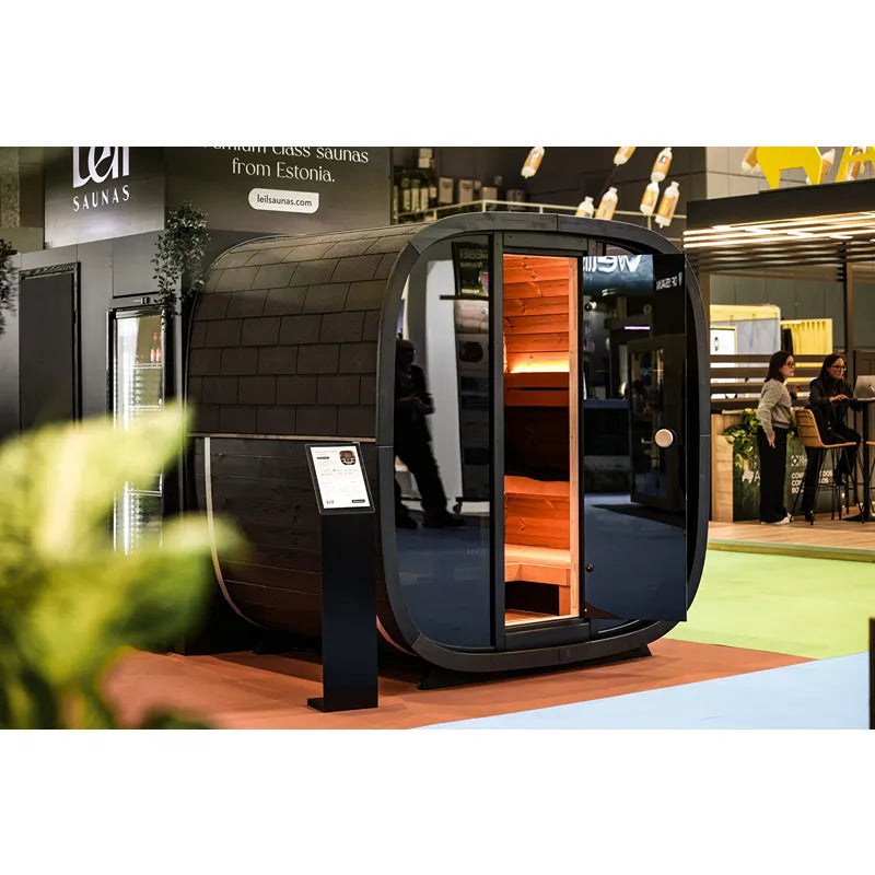 Leil Black Cube Premium Gartensauna Hexagon-Wand mit schwarzem Außenrahmen und orangem Holzinnenraum auf Messe-Messestand