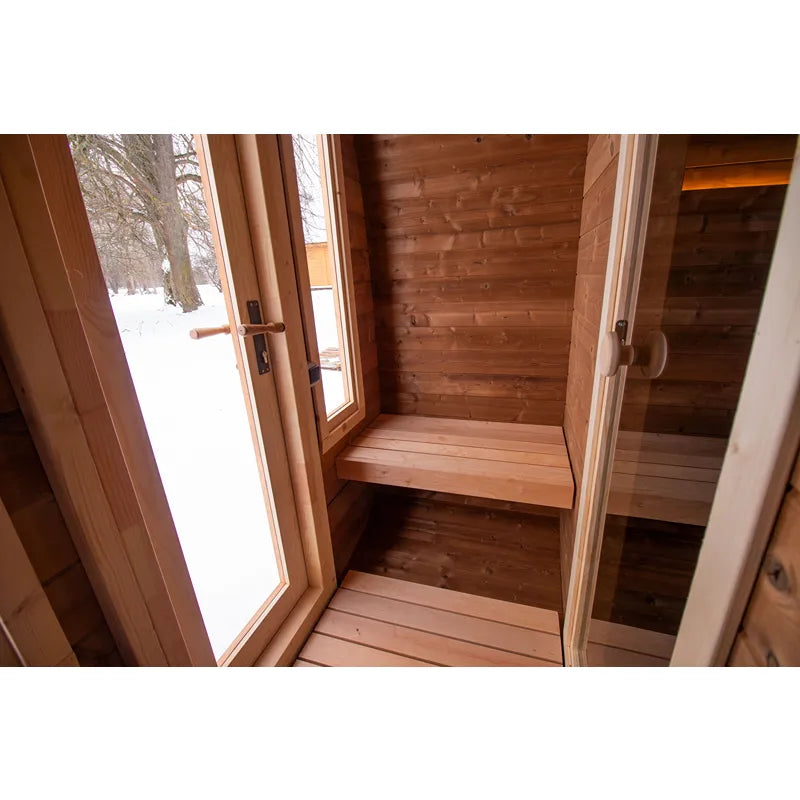 Leil Dice Dual Gartensauna von Leil Saunas – Innenraum mit Holzbänken und geöffneter Eingangstür zum verschneiten Garten