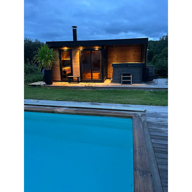 Leil Patio L Plus Gartensauna mit Überdachung von Leil Saunas, abends beleuchtet neben Pool im Garten