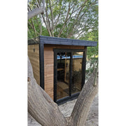 Leil Patio S Gartensauna 4 Personen 4,0 m² mit schwarzem Rahmen und Holzverkleidung im Garten zwischen Bäumen