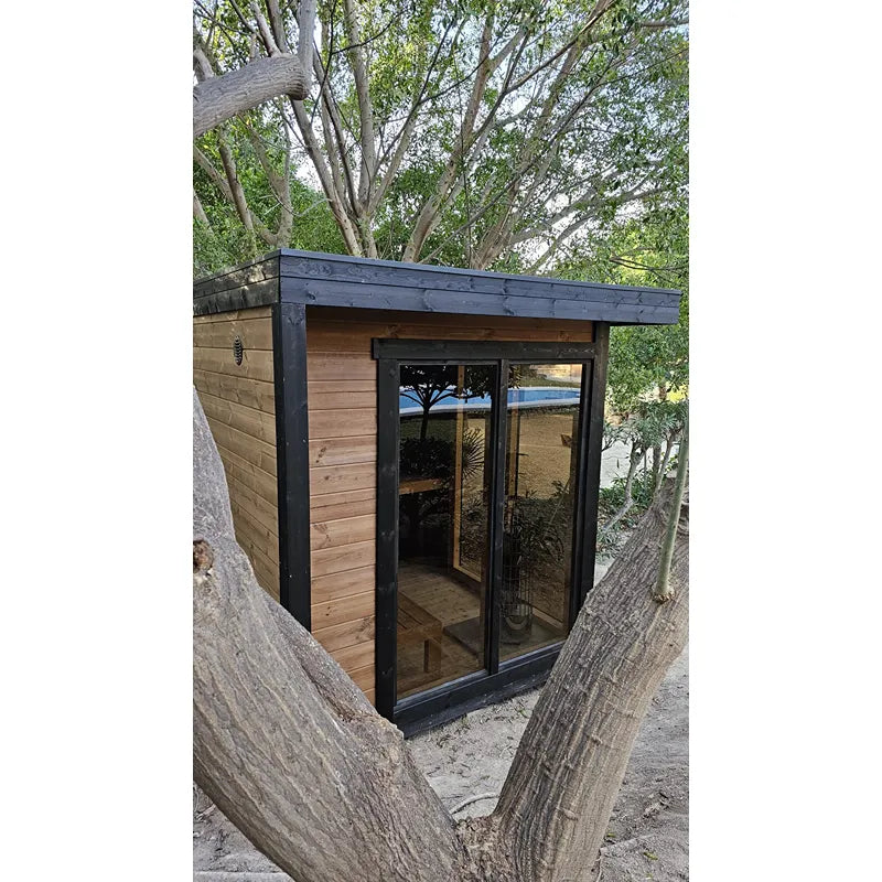 Leil Patio S Gartensauna 4 Personen 4,0 m² mit schwarzem Rahmen und Holzverkleidung im Garten zwischen Bäumen