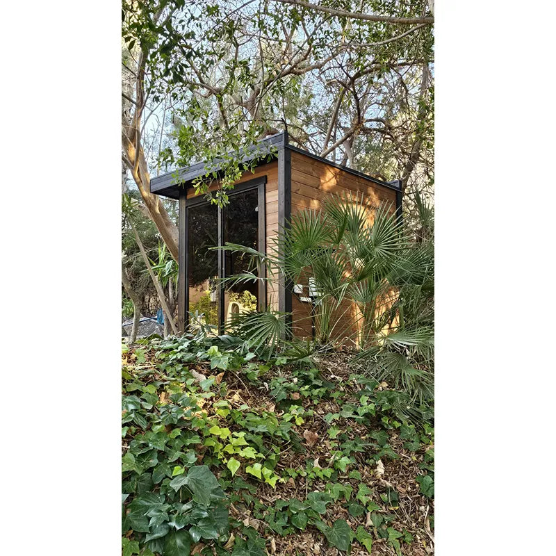 Leil Patio S Gartensauna 4 Personen mit Holzfassade und großem Fenster, umgeben von Garten und Bäumen