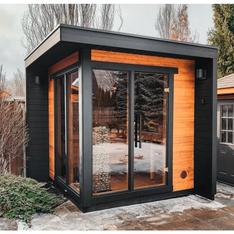 Leil Patio S Gartensauna 4 Personen 4,0 m² von Leil Saunas mit schwarzem Rahmen und orangeholz-Innenausbau im winterlichen Garten