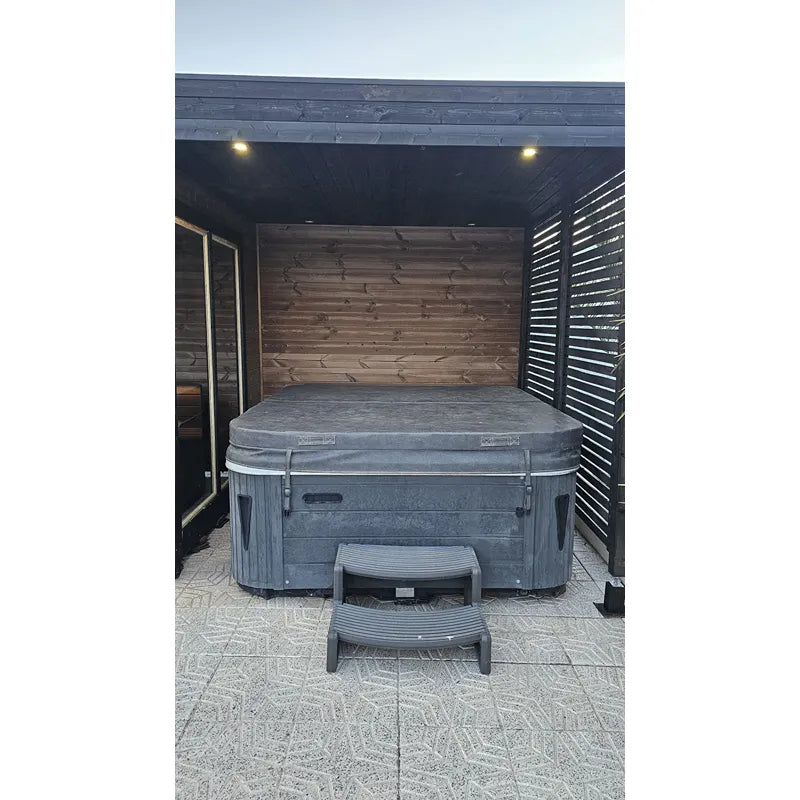 Leil Patio S Plus Gartensauna mit Überdachung, dunkelgraues Holzmodell mit integriertem Whirlpool und Treppeneinstieg unter moderner Terrassenüberdachung