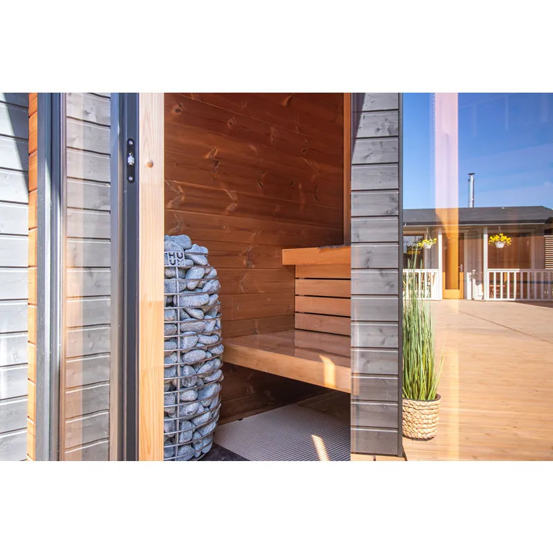 Leil® Patio XS Gartensauna 4 Personen von Leil® Saunas mit offener Tür, Holzinnenraum und Steinofen auf sonniger Terrasse