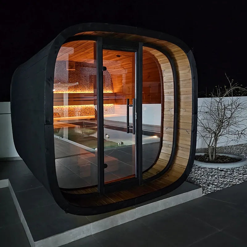 Leil Round Cube Mini Gartensauna 4 Personen von Leil Saunas mit schwarzem Außenrahmen und Holzinnenausstattung in modernem Gartendesign bei Nacht beleuchtet