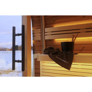 Leil Round Cube Mini – Gartensauna 4 Personen von Leil Saunas mit Holzbänken, schwarzem Handtuch und Eimer im Innenraum, Seenblick durch großes Fenster