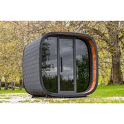 Leil Round Cube Mini – Gartensauna 4 Personen von Leil Saunas mit schwarzem Holzschindel-Design und großem Glasfenster im Garten