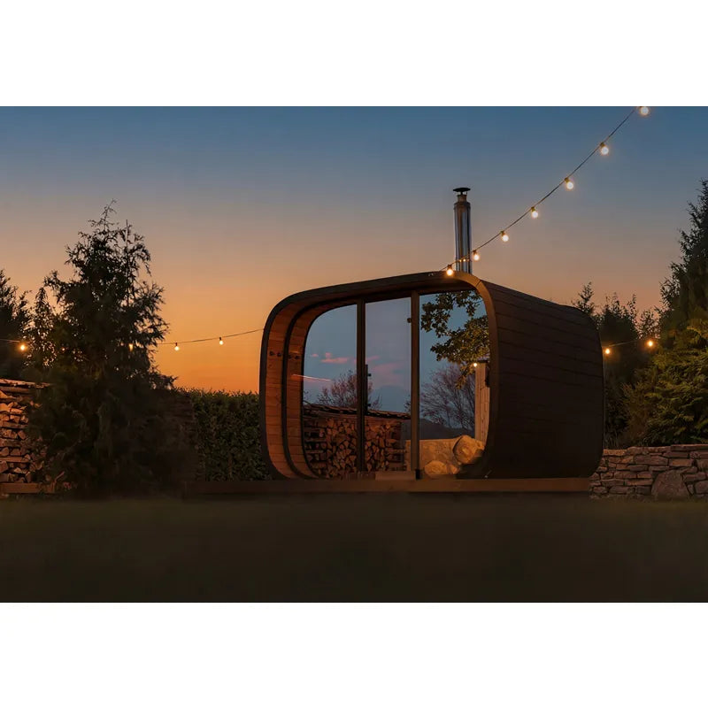 Leil Round Cube Single – Premium Gartensauna 1 Raum von Leil Saunas im Garten bei Dämmerung mit Panoramafenstern und Holzofen