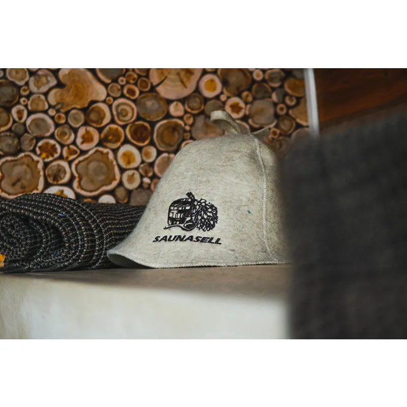 Leil Round Cube Single Gartensauna Saunazubehör – weiße Saunakappe mit Leil Saunas Logo vor Holzquerschnitten