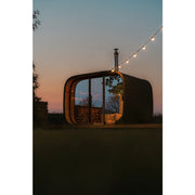 Leil Round Cube Single – Premium Gartensauna 1 Raum von Leil Saunas im Garten bei Sonnenuntergang mit Holzlagerung und Lichterkette