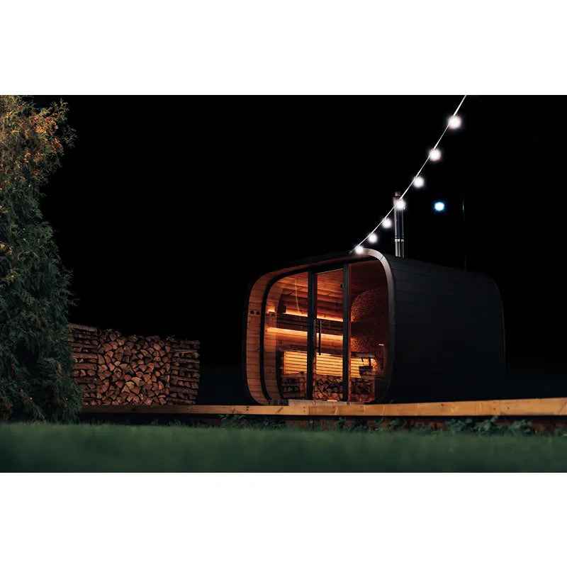 Leil Round Cube Single Premium Gartensauna 1 Raum mit beleuchteter Holzfassade und Panoramafenster im Garten bei Nacht