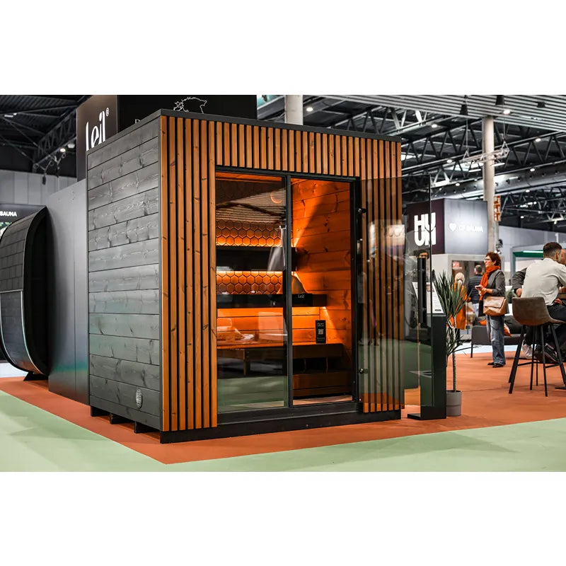 Leil® Viva 210 Gartensauna 4 Personen mit Liege von Leil® Saunas auf Messe, moderne Holzfassade mit vertikalem Design und großer Glasfront