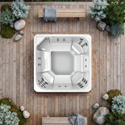 Novitek L-0 Outdoor Whirlpool von oben auf Holzterrasse, umgeben von Pflanzen und Steinen, Draufsicht eines quadratischen Whirlpools mit Düsen und Sitzbereichen