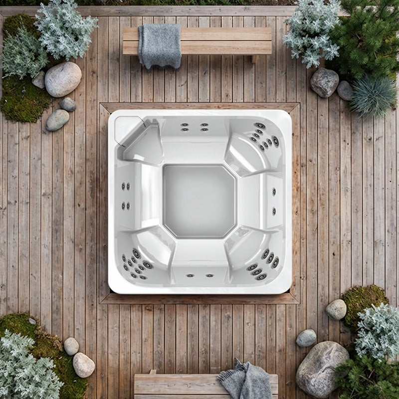 Novitek L-0 Outdoor Whirlpool von oben auf Holzterrasse, umgeben von Pflanzen und Steinen, Draufsicht eines quadratischen Whirlpools mit Düsen und Sitzbereichen