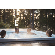 Familie genießt entspannende Zeit im Novitek S-0 Outdoor Whirlpool vor Waldkulisse bei Sonnenuntergang
