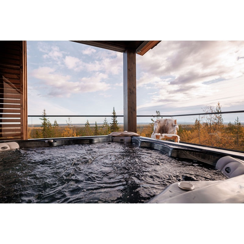Novitek M-1 Outdoor Whirlpool mit sprudelndem Wasser auf einer Terrasse mit Panoramablick auf bewaldete Landschaft und Himmel