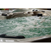 Whirlpool mit aufgewühltem grünem und weißem Wasser in vollem Betrieb, beige Kunststoffwanne mit Düsen und schwarzen Griffen sichtbar