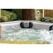 Passion Elevate Eisbad mit sprudelndem türkisblauem Wasser und schwarzen Nackenkissen in Gartenumgebung mit Baumstamm und Moos