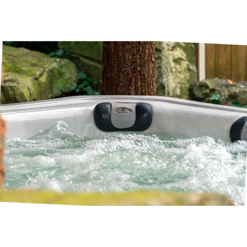 Passion Elevate Eisbad mit sprudelndem türkisblauem Wasser und schwarzen Nackenkissen in Gartenumgebung mit Baumstamm und Moos