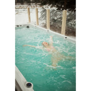 Passion Spas Activity 2 Swim Spa für 3 Personen - Person schwimmt in türkisblauem Wasser mit Gegenstromanlage im Garten bei Schnee