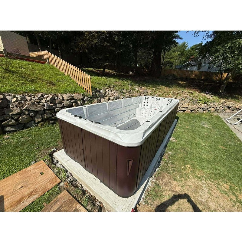 Im Garten integrierter Passion Spas Activity 2 Swim Spa mit brauner Außenverkleidung auf Betonfundament.