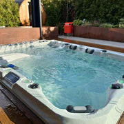Passion Spas Ecstatic Whirlpool mit türkisblauem Wasser, weißem Rand, Düsen und Steuerelementen in einem modernen Terrassen-Garten mit grünen Hecken und Holzverkleidung.