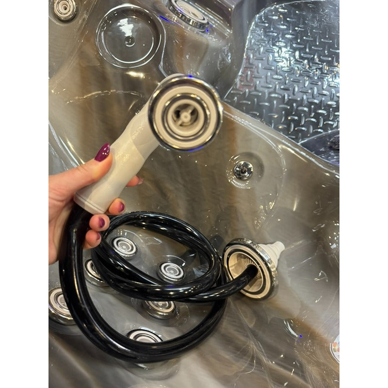 Passion Spas Freestyle Massage Jet in Weiß mit schwarzem Anschlussschlauch, in Hand gehalten über Whirlpool-Düsen