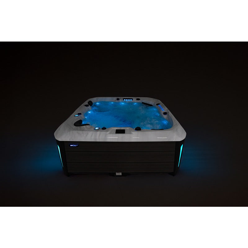 Platinum Spas Barcelona Outdoor Whirlpool mit beleuchtetem Wasserbecken, grauem Rand und schwarzem Unterschrank vor dunklem Hintergrund