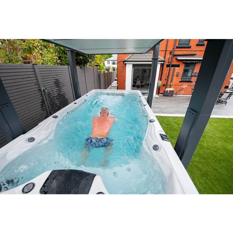 Mann schwimmt im Platinum Spas Eros Swim Spa – Demonstration der Gegenstromfunktion im Außenbereich unter einer Überdachung