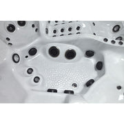 Innenansicht eines Whirlpools mit weißem Kunststoffbecken, zahlreichen schwarzen Massagedüsen und strukturiertem Bodenbelag zum Einstieg, Draufsicht auf die Liegebereiche und Sitzbereiche.