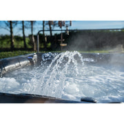 Platinum Spas Maximus Outdoor Whirlpool mit sprudelndem Wasser und Luftdüsen, umgeben von grünem Garten und klarem Himmel