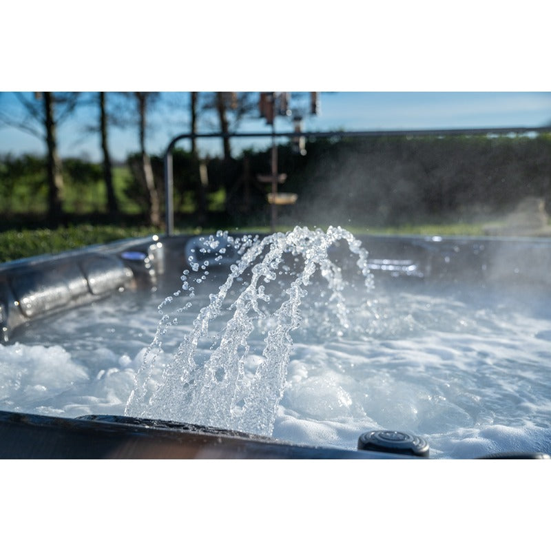 Platinum Spas Maximus Outdoor Whirlpool mit sprudelndem Wasser und Luftdüsen, umgeben von grünem Garten und klarem Himmel