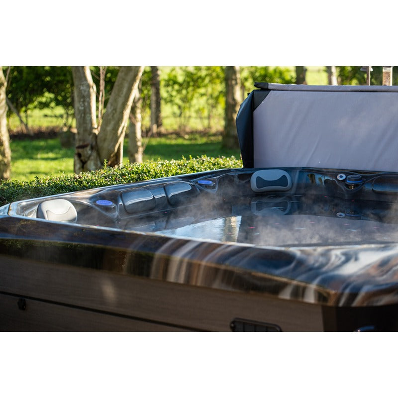 Platinum Spas Maximus Outdoor Whirlpool mit offener Abdeckung und Wasserdüsen vor grüner Gartenkulisse mit Bäumen