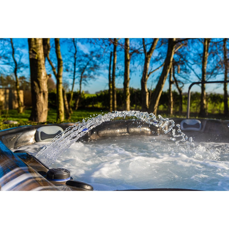 Platinum Spas Maximus Outdoor Whirlpool mit sprudelndem Wasser im Freien, umgeben von Bäumen und grüner Landschaft bei Tageslicht.