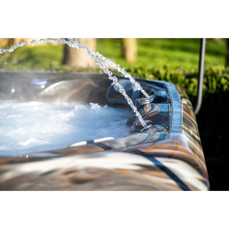 Wasser läuft aus einem Whirlpool Platinum Spas Maximus mit aufgewärmtem Wasser in den Garten, im Hintergrund grüne Hecke