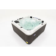 Platinum Spas Palma Outdoor Whirlpool mit weißem Rand, dunkelbraunem Holzdekor-Gehäuse und sprudelndem Wasser für bis zu 6 Personen.