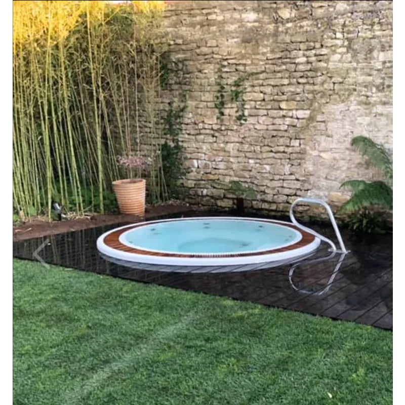 Portcril Club 25 Overflow Spa 7-Personen Whirlpool mit braunem Holzrand, eingelassen im Garten neben Steinmauer
